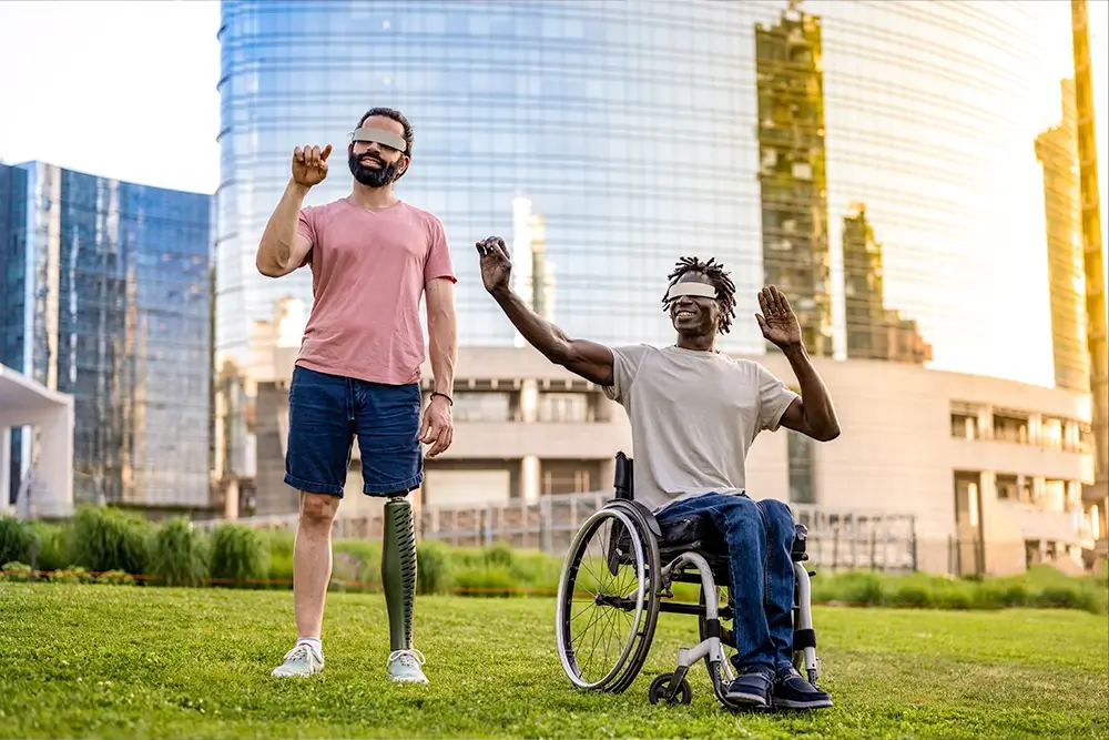 a man with prosthetic leg and a man sitting in a wheel chair interacting with virtual reality with their virtual goggles on